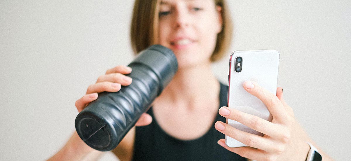 foto de mujer sosteniendo un smartphone blanco y botella deportiva